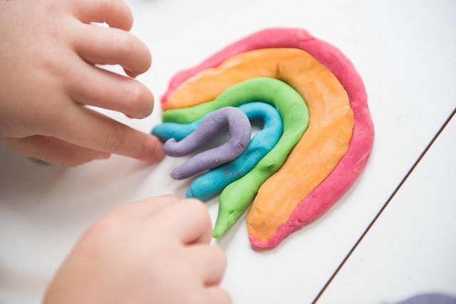 Two child's hand making a rainbow out of playdough.