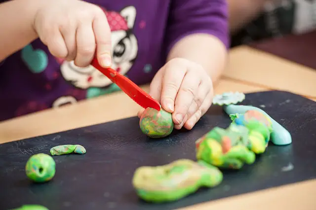 Child cutting playdough with plastic knife.
