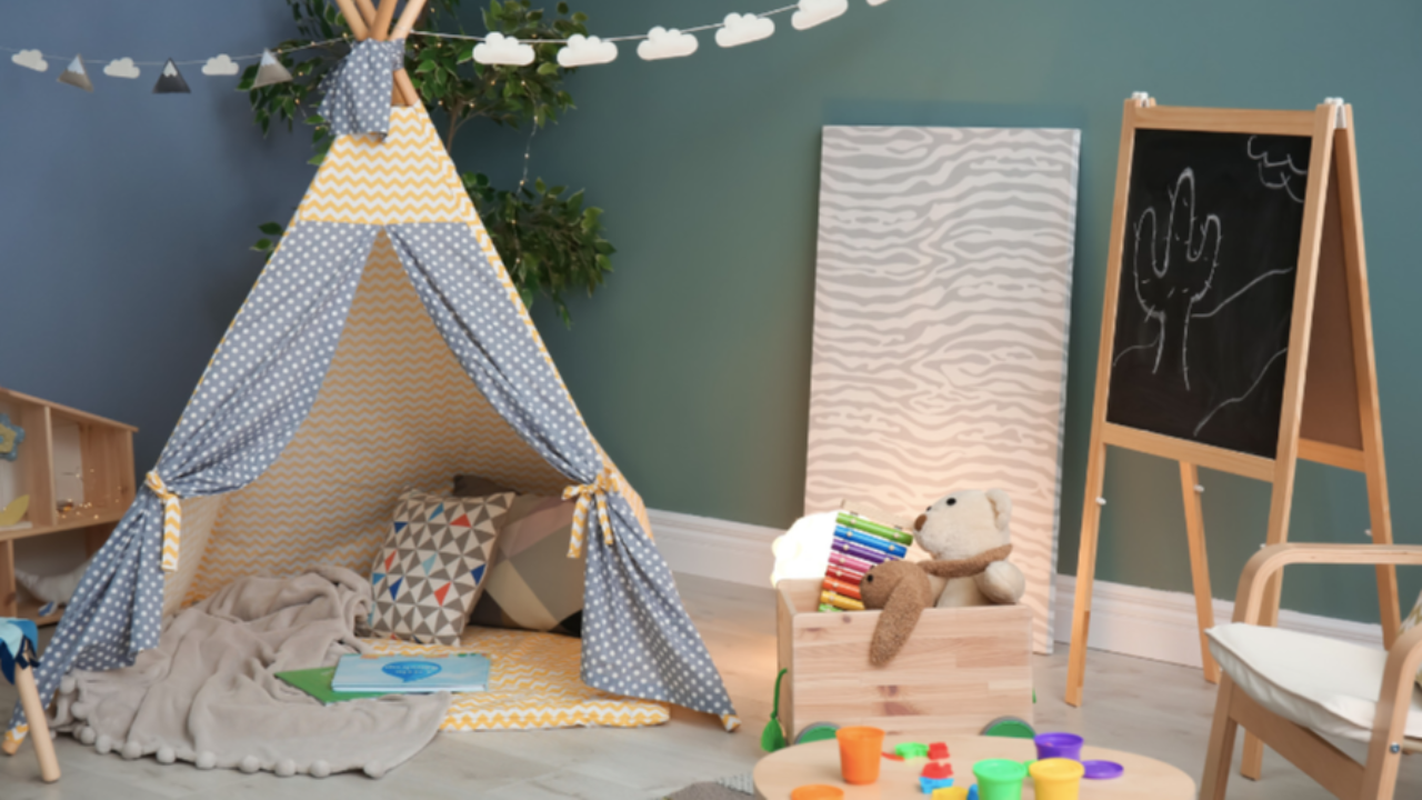 Cozy calming space for kids with a fabric teepee, pillows, stuffed bear, art supplies, and a small chalkboard in a playroom.