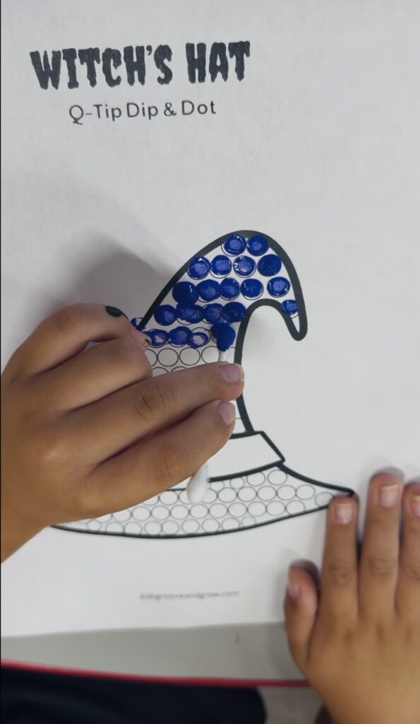 Child painting a witch’s hat Q-tip fine motor worksheet using blue paint dots
